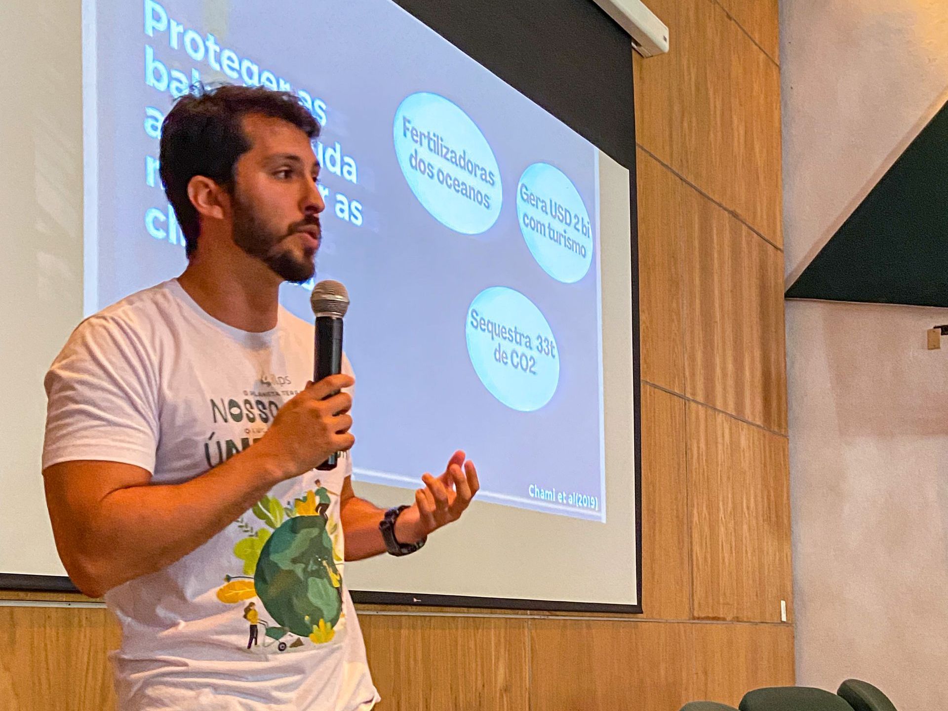 Um homem está segurando um microfone na frente de uma tela de projetor.