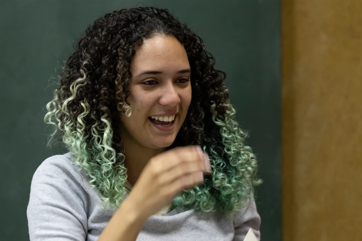 Uma mulher com cabelos cacheados e mechas verdes está sorrindo.