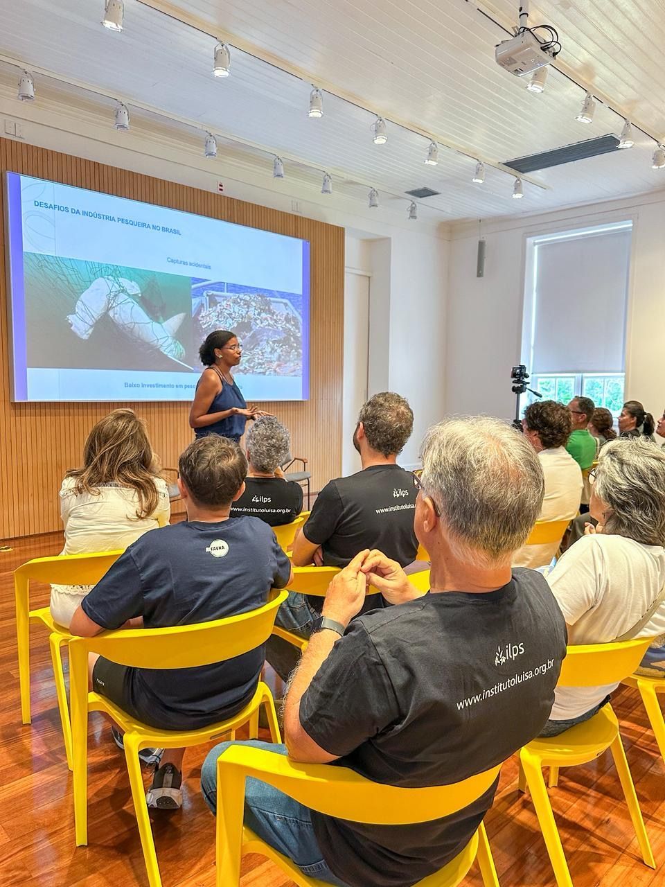 Um grupo de pessoas está sentado em uma sala de aula assistindo a uma apresentação.