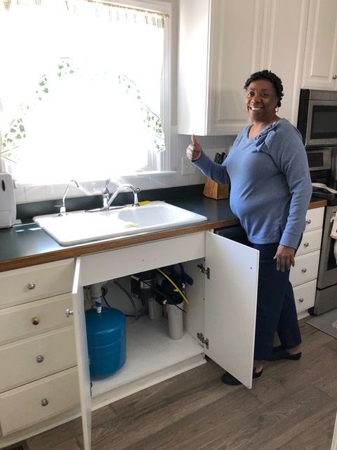 A woman is giving a thumbs up in front of a kitchen sink