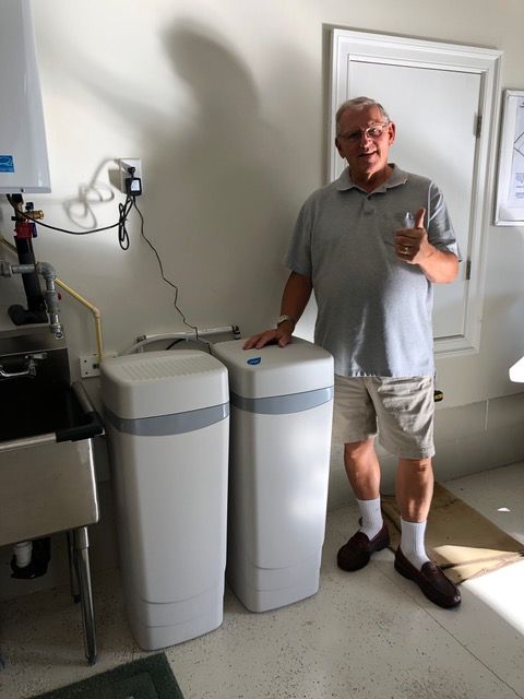 A man is standing in a room next to two water tanks and giving a thumbs up.