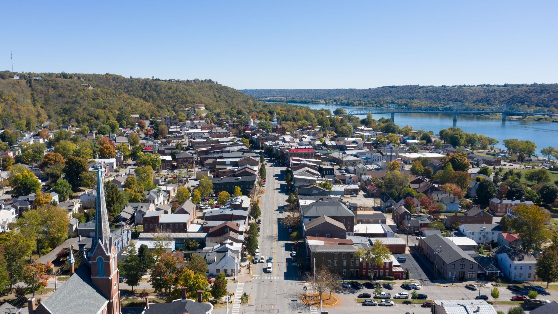 Aerial view of a suburban neighborhood with a lake, hills, and a clear blue sky.
