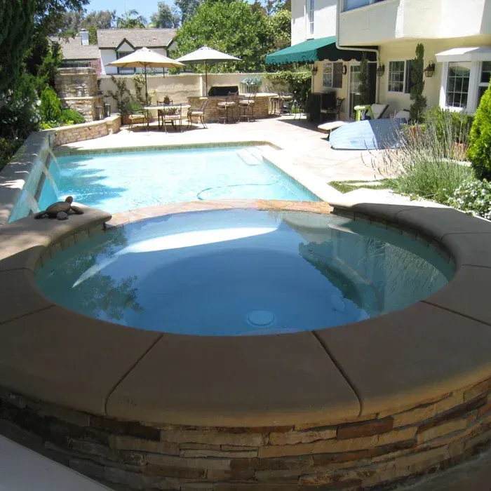Backyard patio with a swimming pool and circular hot tub, surrounded by lounge chairs and greenery