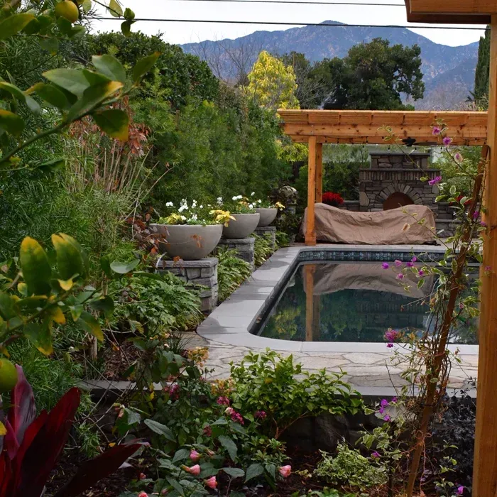 Tropical garden with a small pool, wooden pergola, lush plants, and mountain view in the background