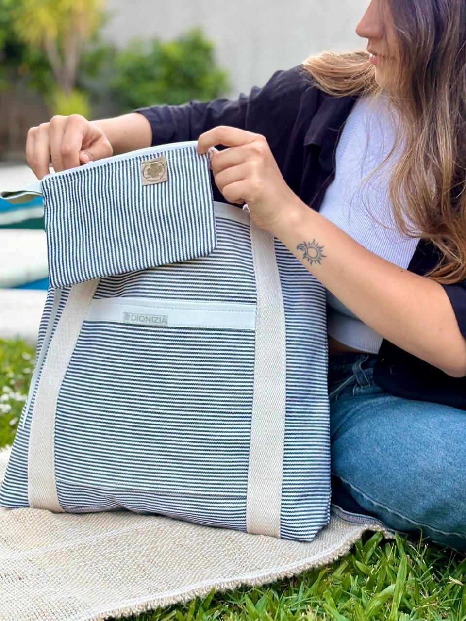 Mujer sentada en el césped con un bolso de rayas, cerca de una piscina.