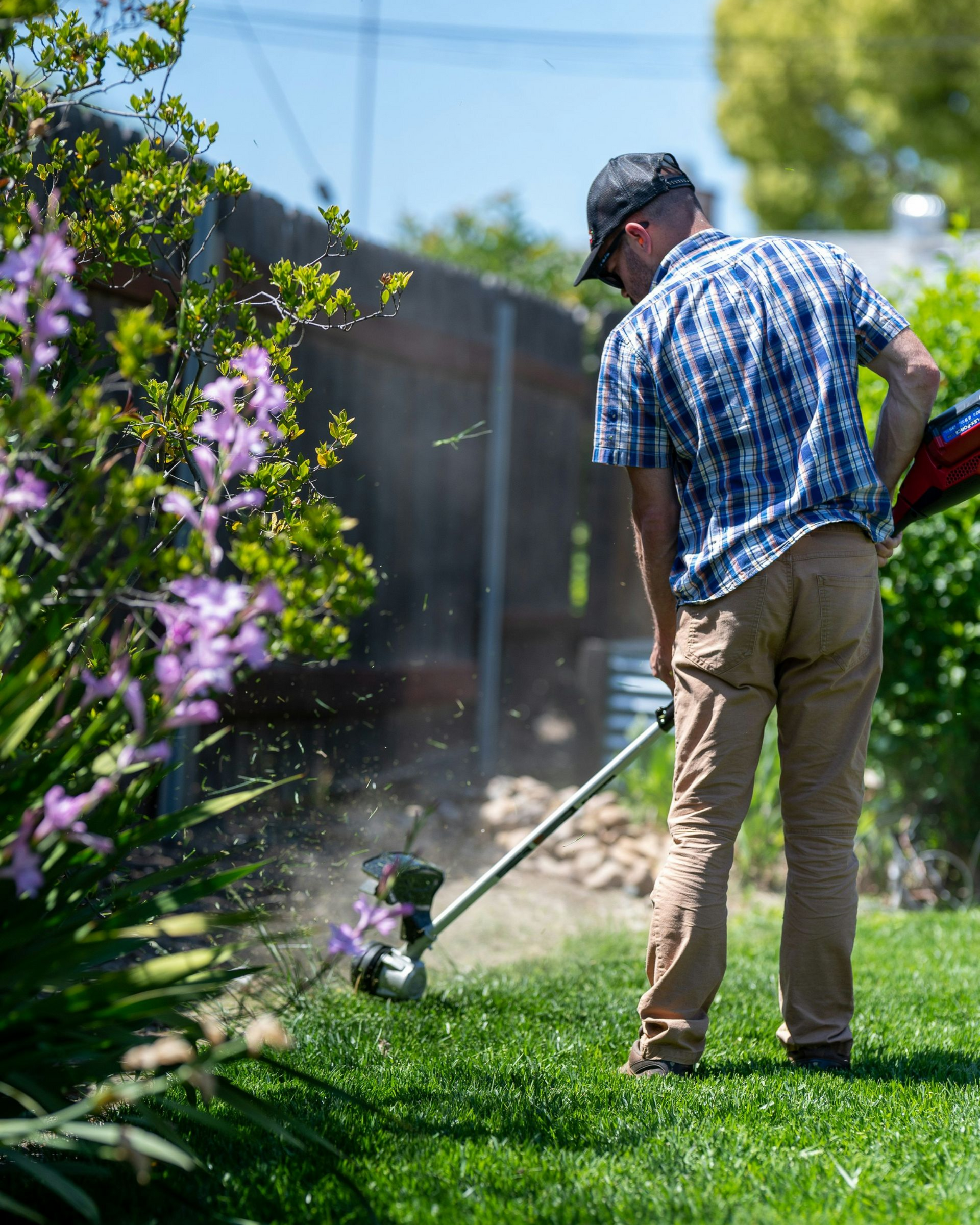 Person using a string trimmer to cut grass in a sunny backyard garden