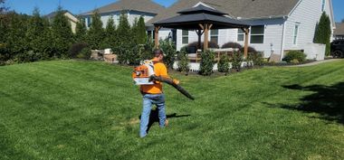 Worker using a leaf blower on a grassy lawn in front of a house