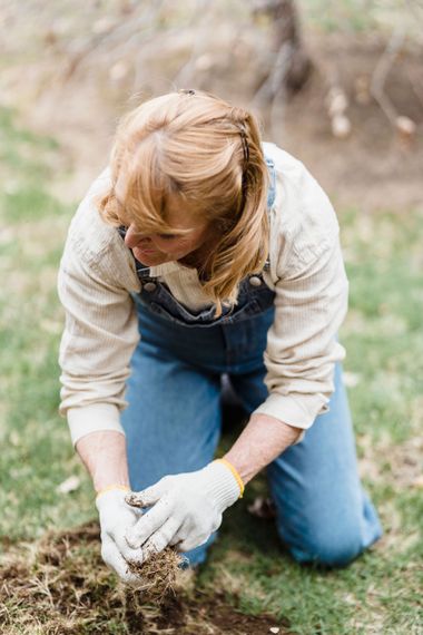 Person kneeling outdoors, planting a small seedling with gloved hands