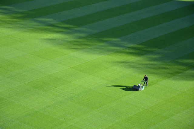 Two groundskeepers mowing a bright green golf course, leaving striped grass patterns