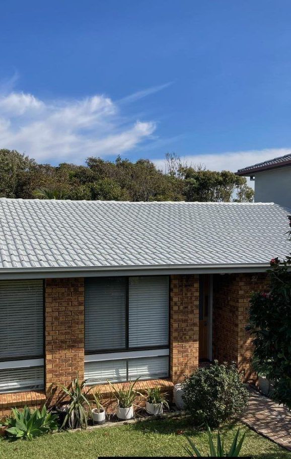 A brick house with a white roof and a blue sky in the background. — Wayne Treasure Roofing & Restoration In Old Bar, NSW