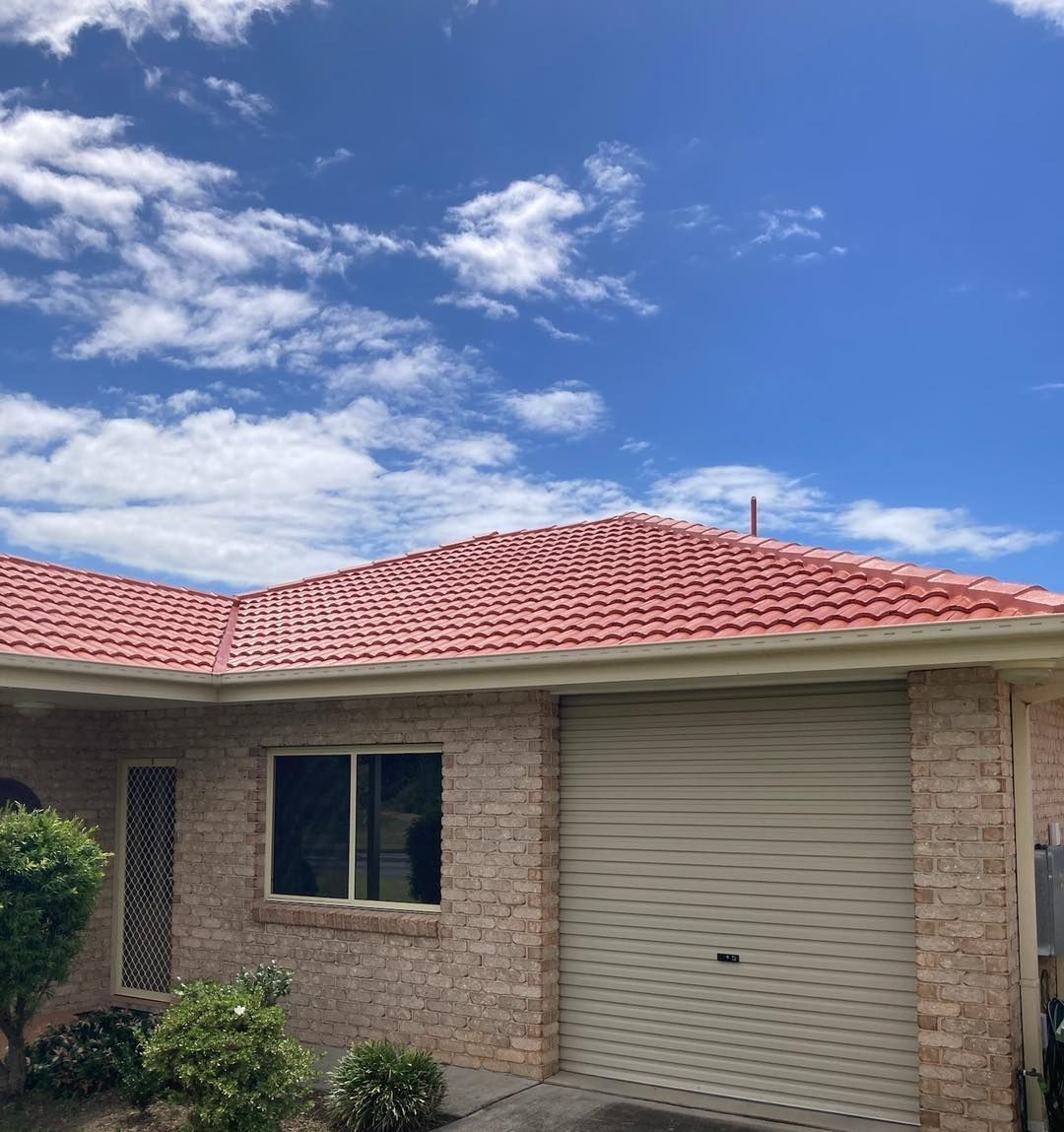 A brick house with a red roof and a white garage door. — Wayne Treasure Roofing & Restoration In Forster, NSW