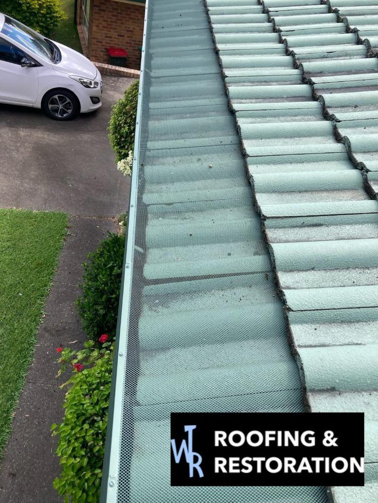 A white car is parked in a driveway next to a gutter on a roof. — Wayne Treasure Roofing & Restoration In Forster, NSW