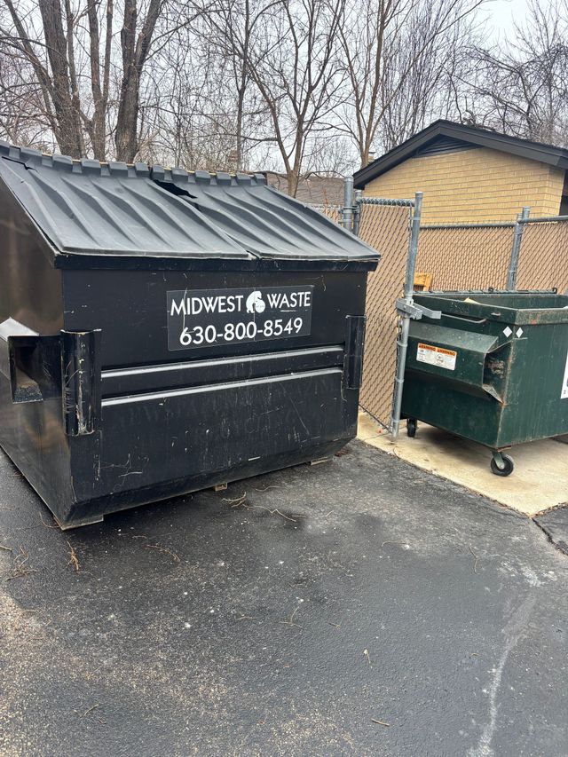 Close-up of a black trash bin filled with black garbage bags, next to green recycling bins outdoors.