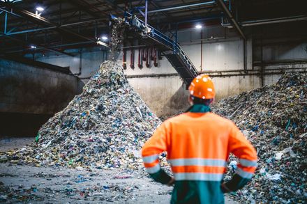 A man is standing in front of a pile of trash in a warehouse.