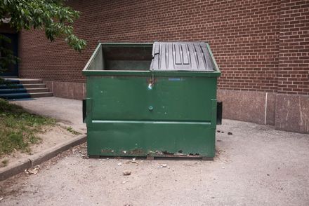 A green dumpster is sitting in front of a brick building