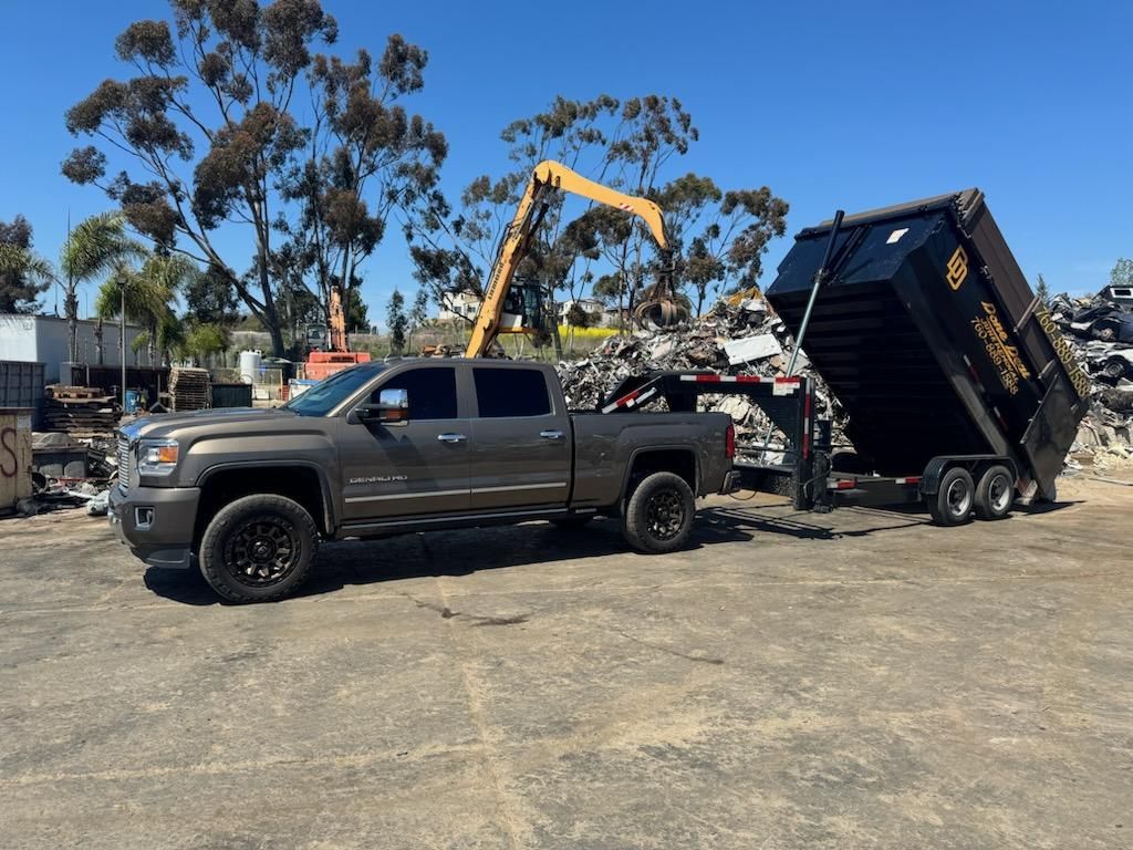 A truck is dumping scrap metal out of the Done Deal Junk Removal trailer into a metal recycling yard.