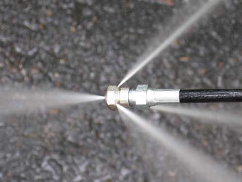 A close up of a hose spraying water on the ground.