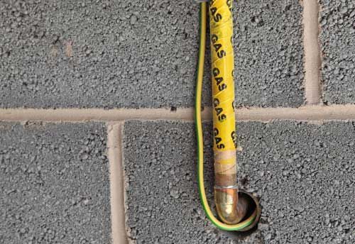 A yellow gas pipe is attached to a brick wall.