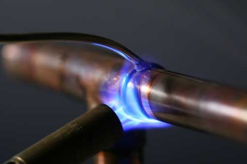 A person is welding a copper pipe with a torch.