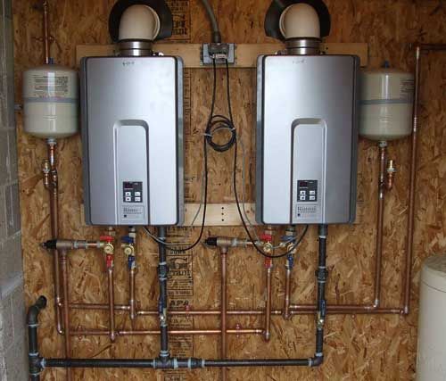 Two water heaters are hanging on a wall next to copper pipes.