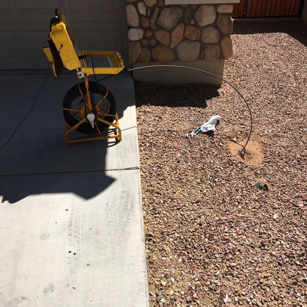 A yellow machine is sitting on the sidewalk next to a stone wall.
