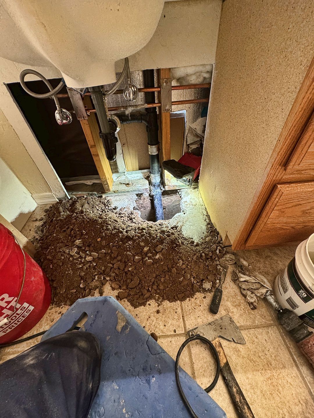 A person is digging a hole under a sink in a bathroom.