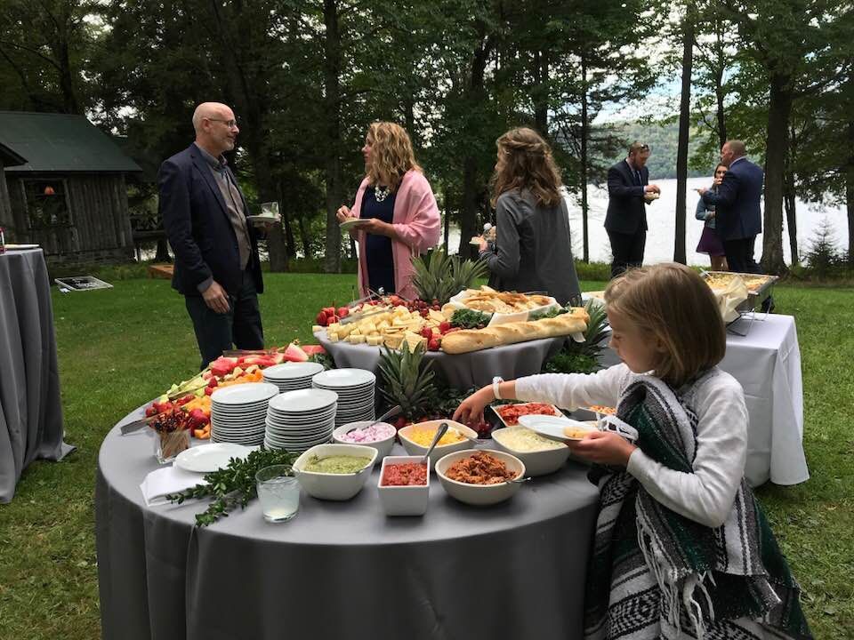 a group of people are standing around a table with food on it .