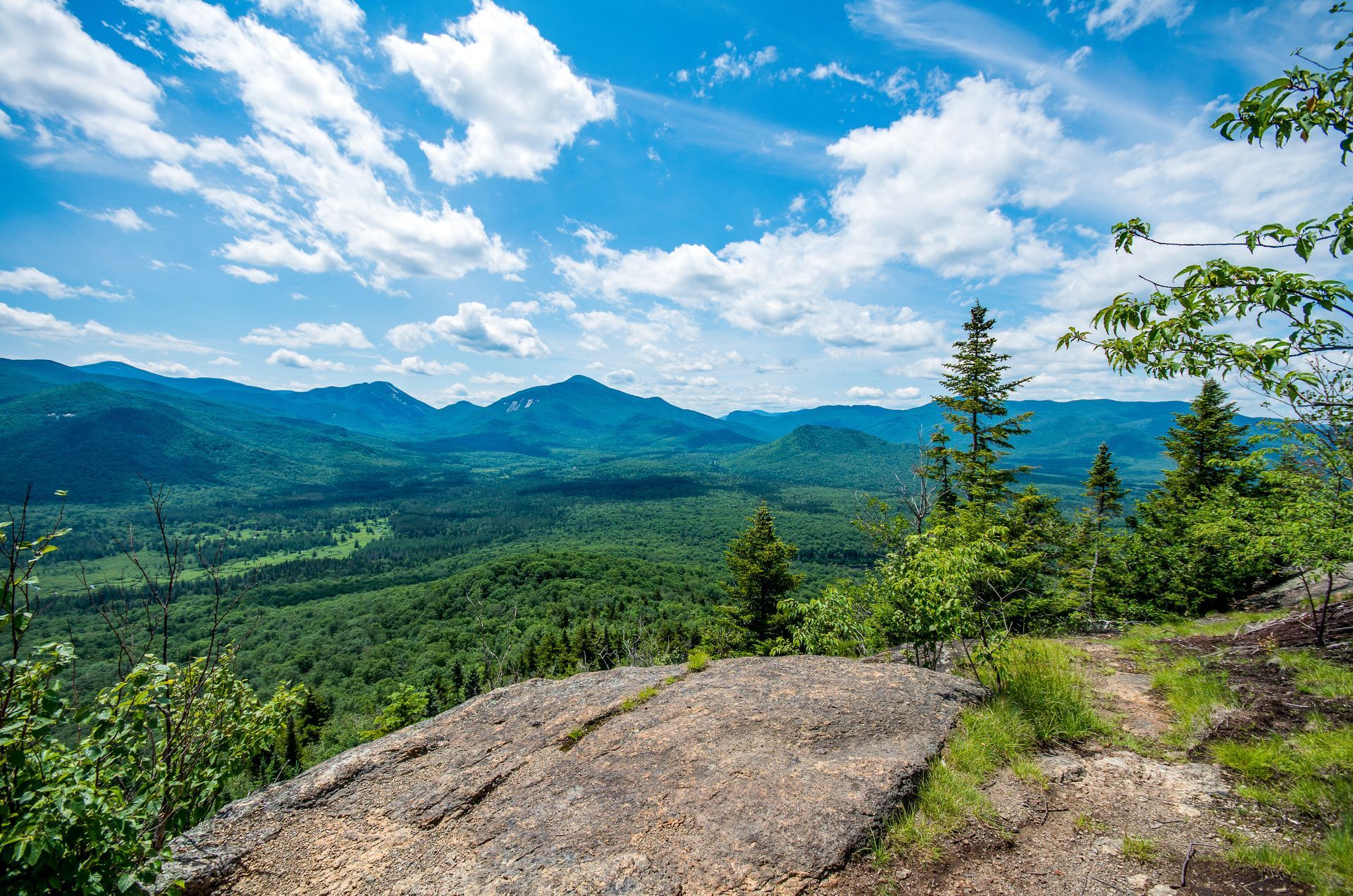 A view of a valley from a rocky cliff with mountains in the background.