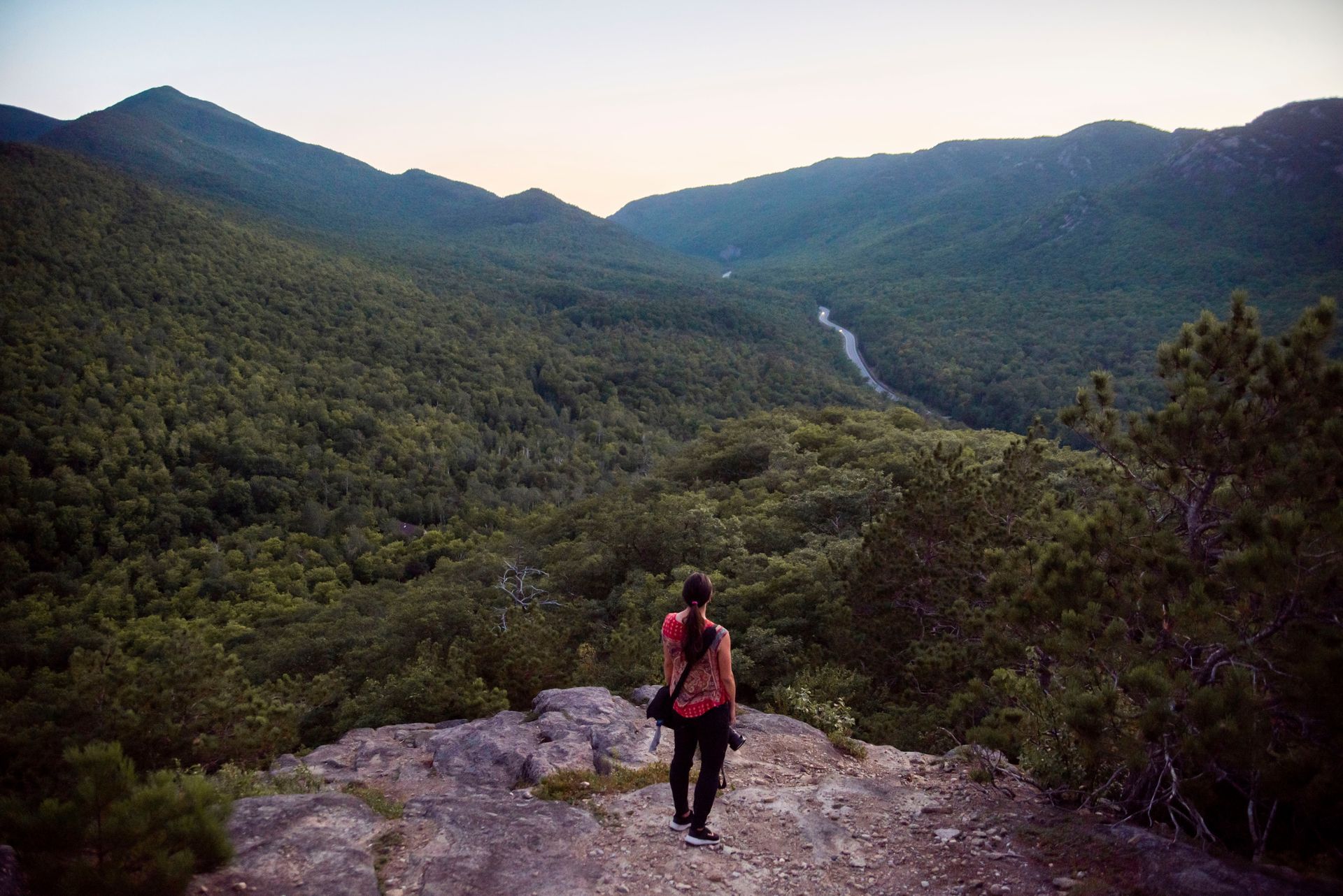 A woman is standing on top of a mountain looking at a river.