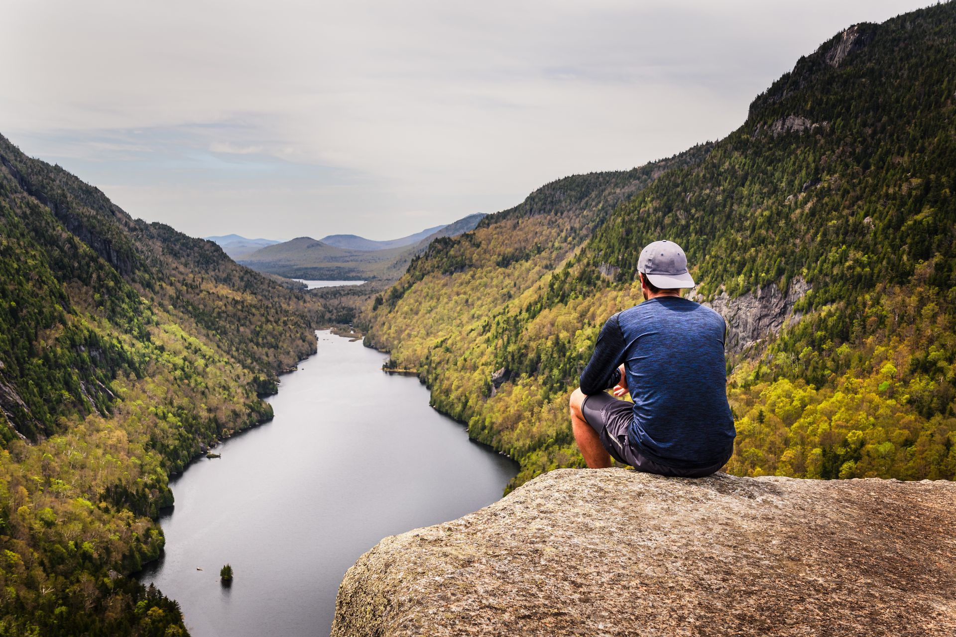 A man is sitting on a rock overlooking a river.