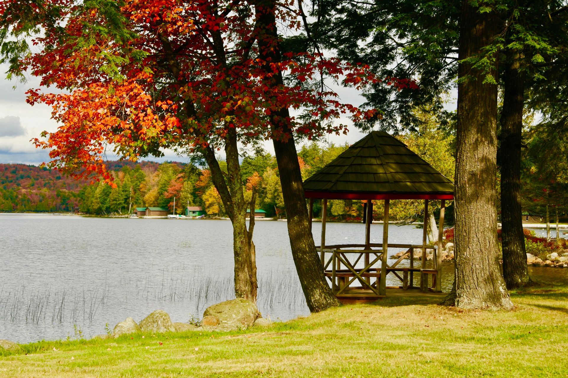 a gazebo sits on the shore of a lake surrounded by trees