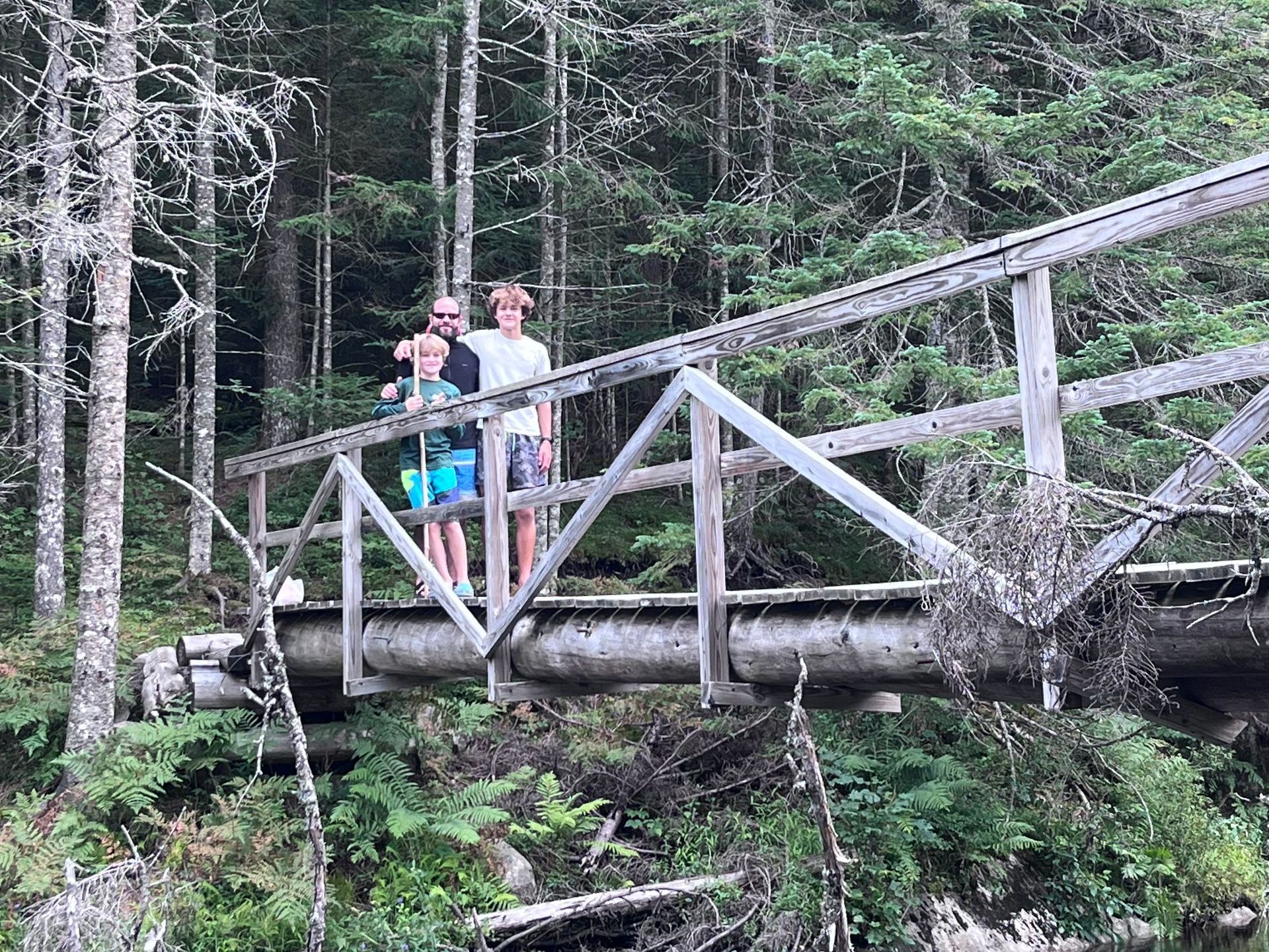 three people on a bridge in the woods