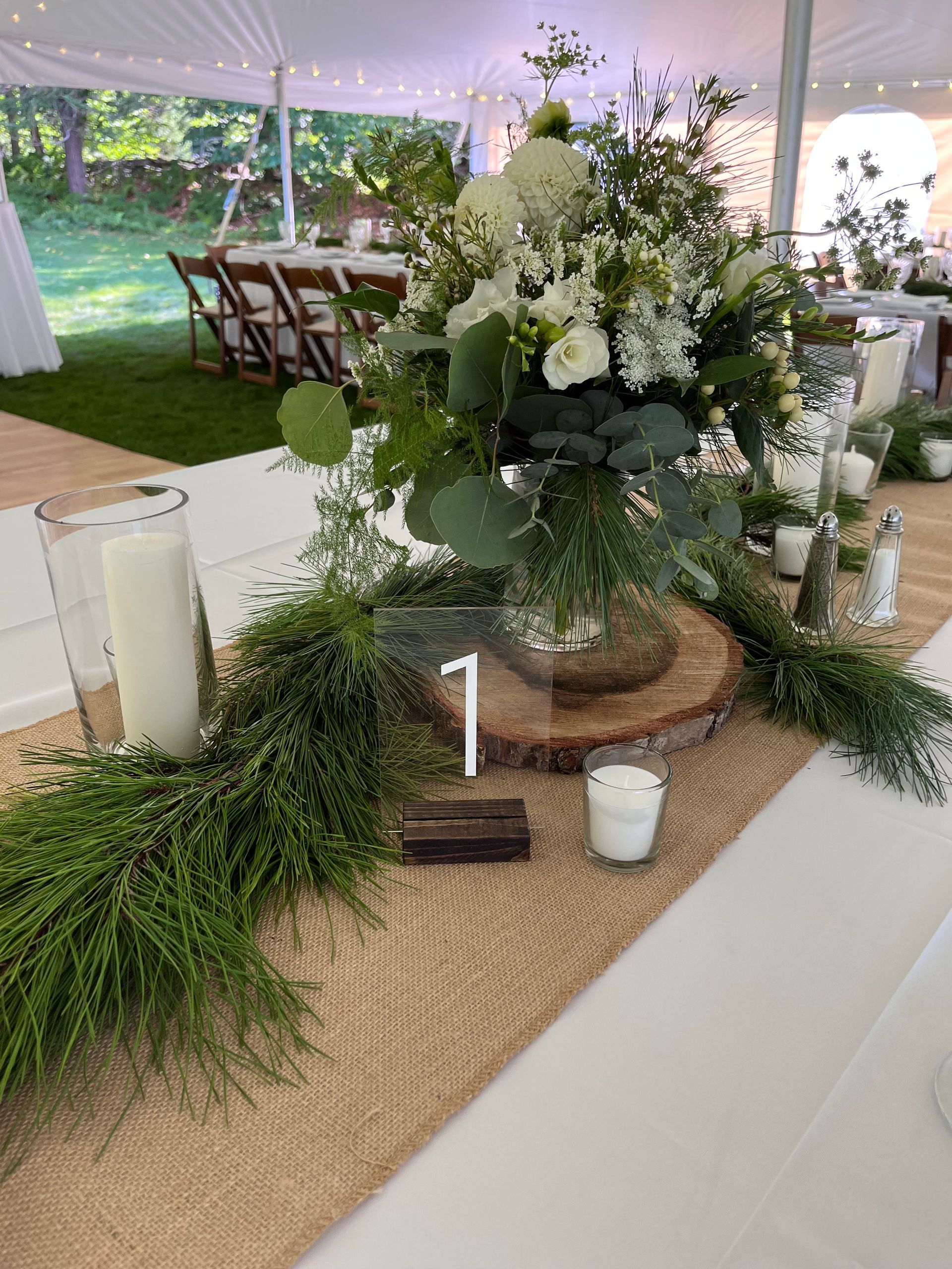 flowers and evergreen boughs on a white table cloth with candles