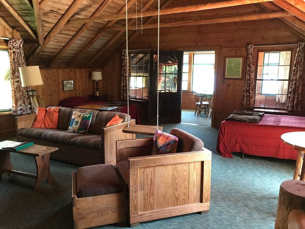 a living room in a log cabin with a couch , chair , table and bed .