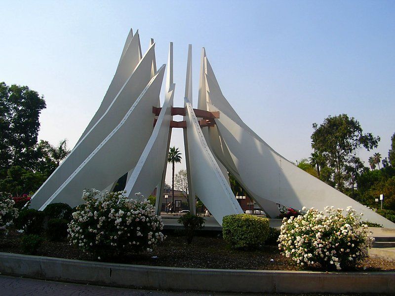 White concrete abstract sculpture with triangular elements in a plaza.
