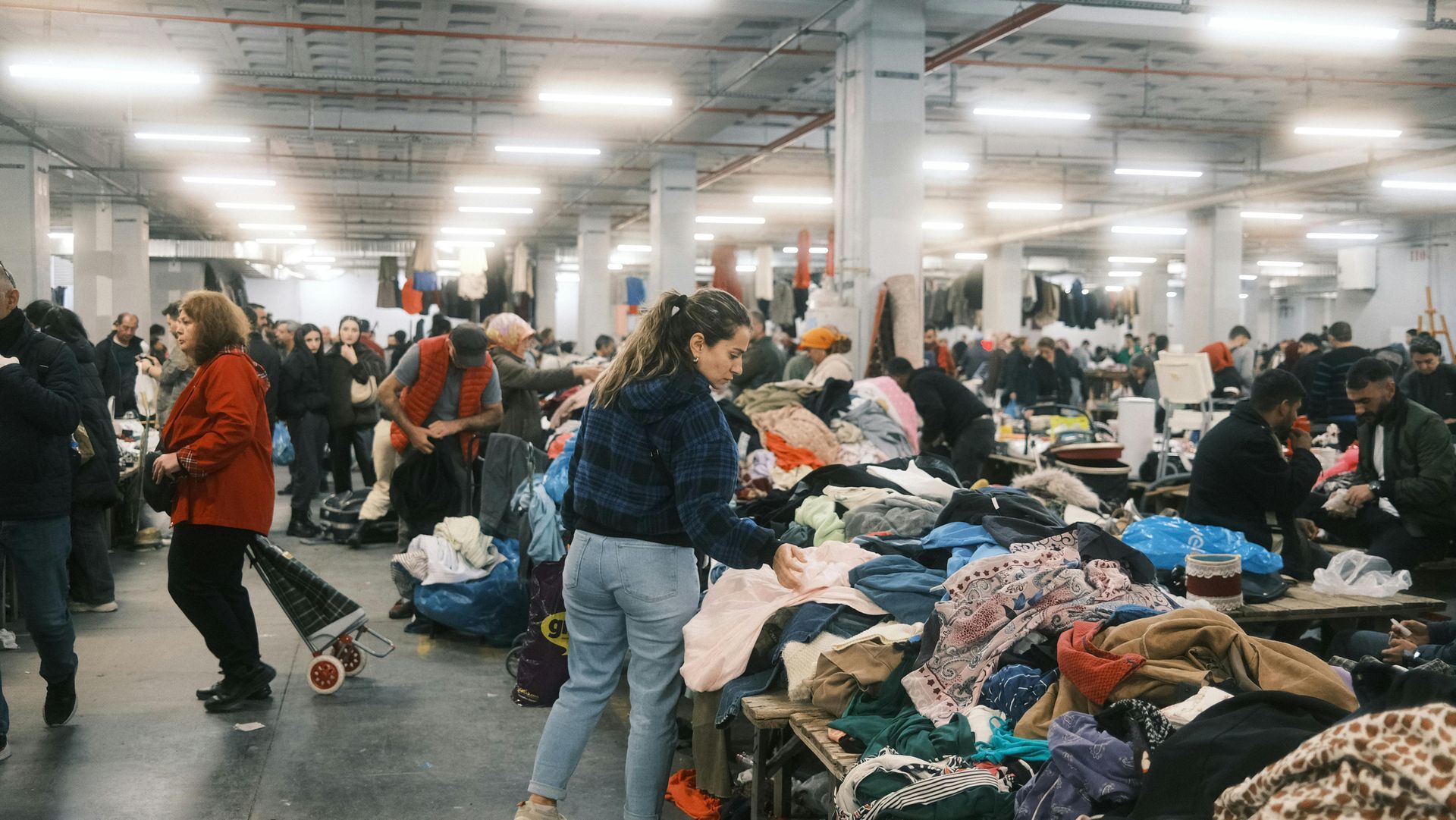 People sorting through clothing in a large indoor space, possibly a shelter or distribution center.