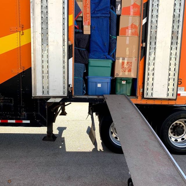 A moving truck is loaded with boxes and a ramp