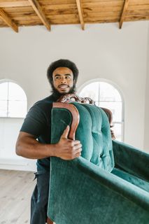 A man is carrying a green couch in a room.