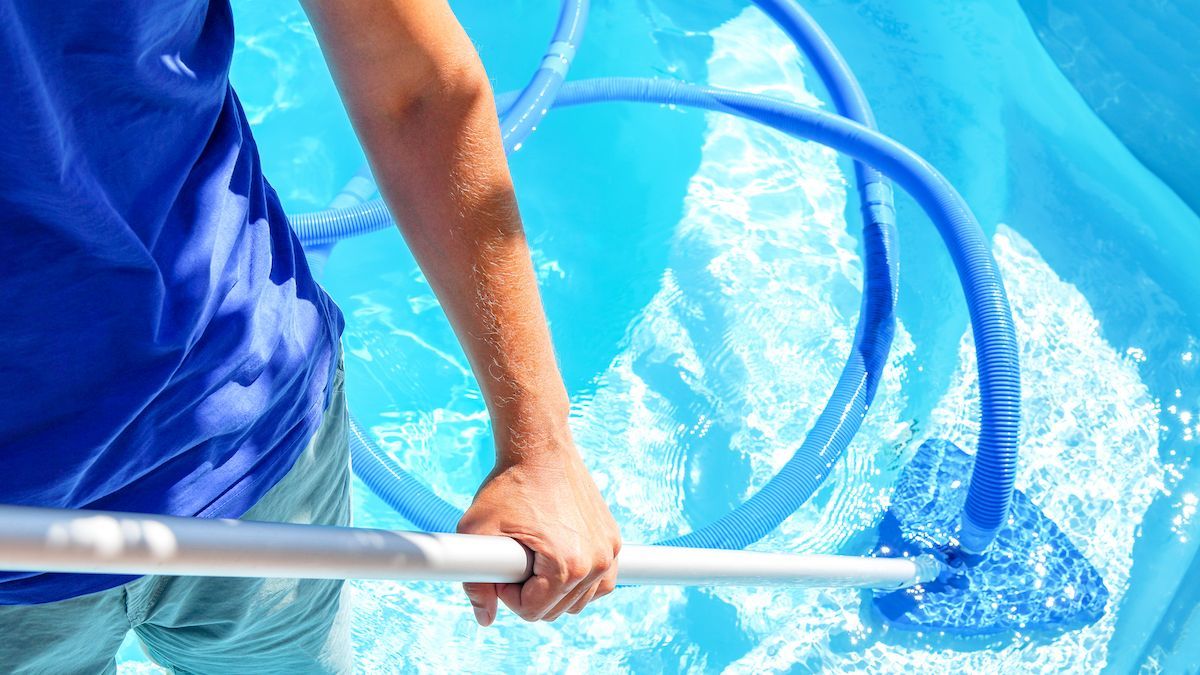 Person cleaning a pool with a blue vacuum, blue water, and sunny day.