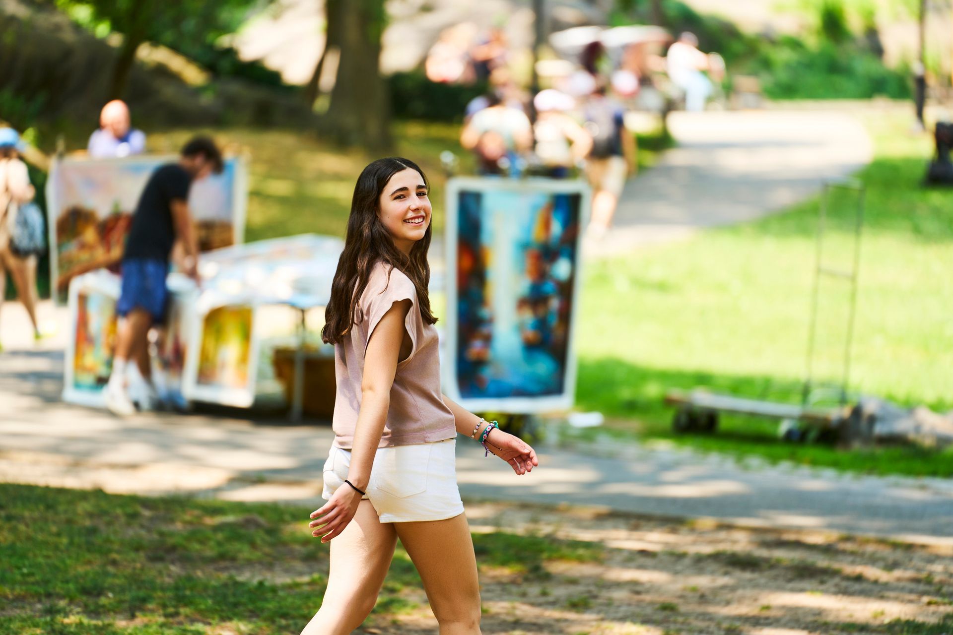 Woman smiling and walking through an outdoor art fair on a sunny day.