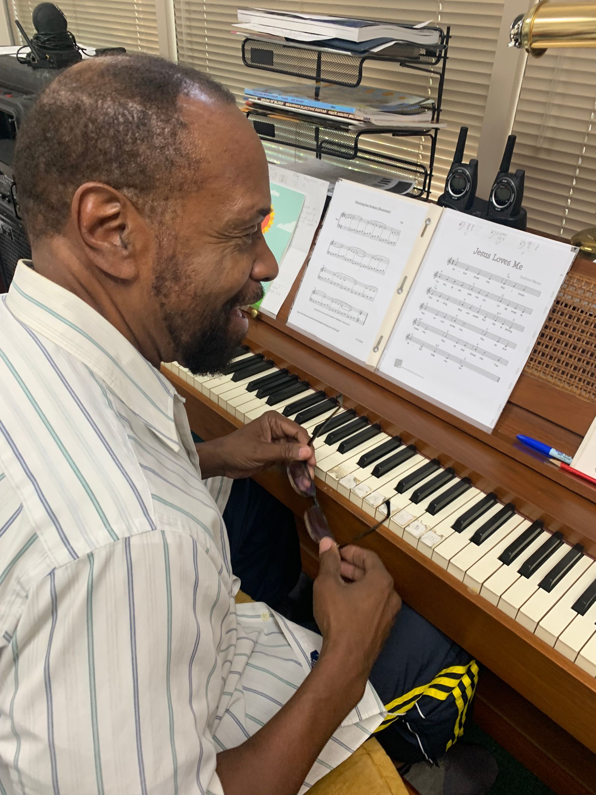 Man playing an organ, smiling. He wears a striped shirt, glasses, and sits in front of sheet music.