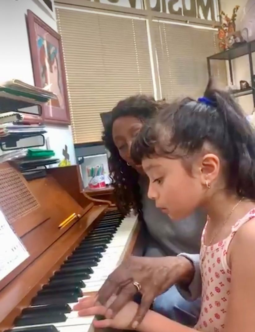 Woman teaching piano to a young girl, both focused on the keys, indoors.
