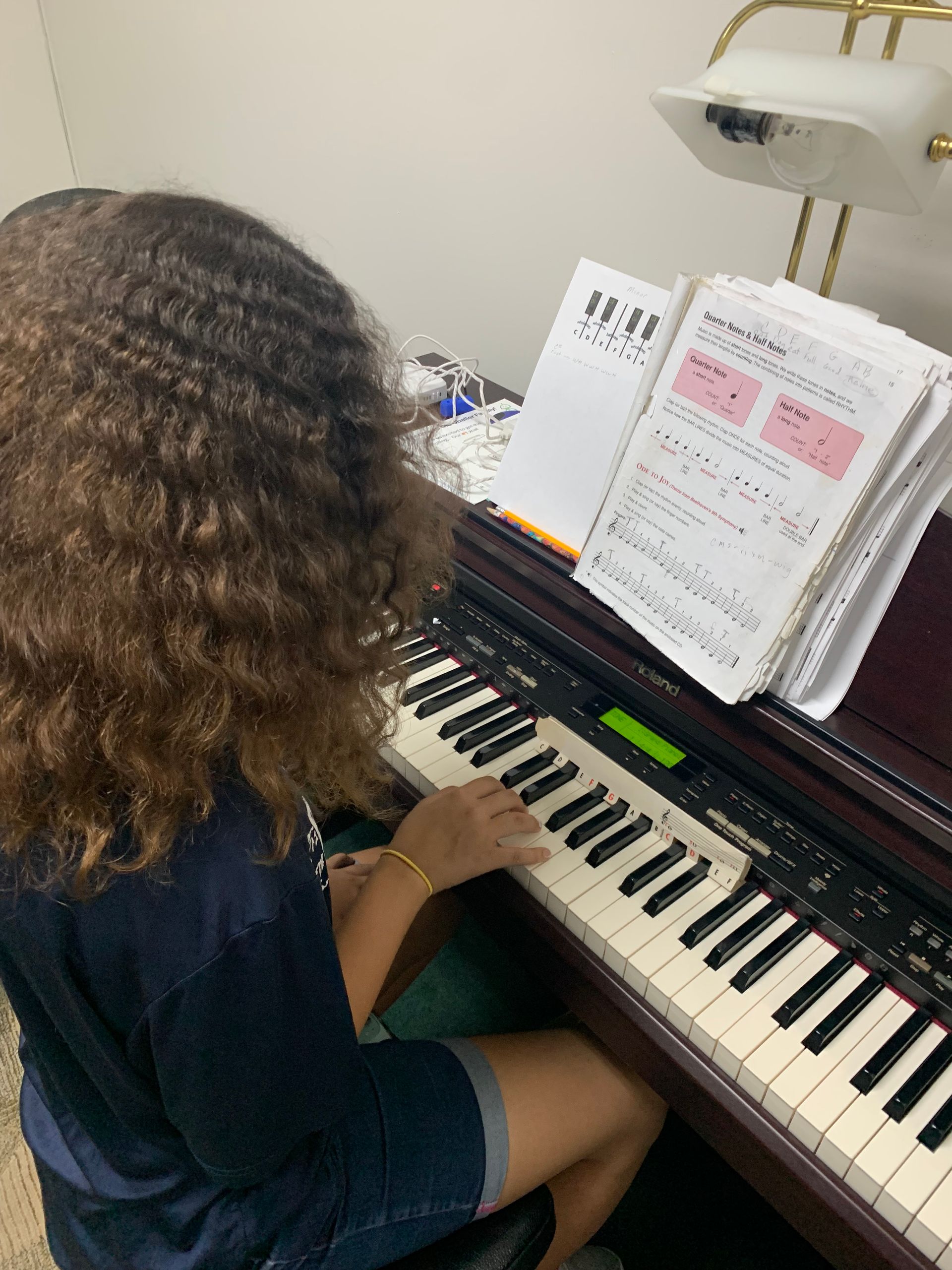 Person with curly hair playing piano, reading sheet music indoors.