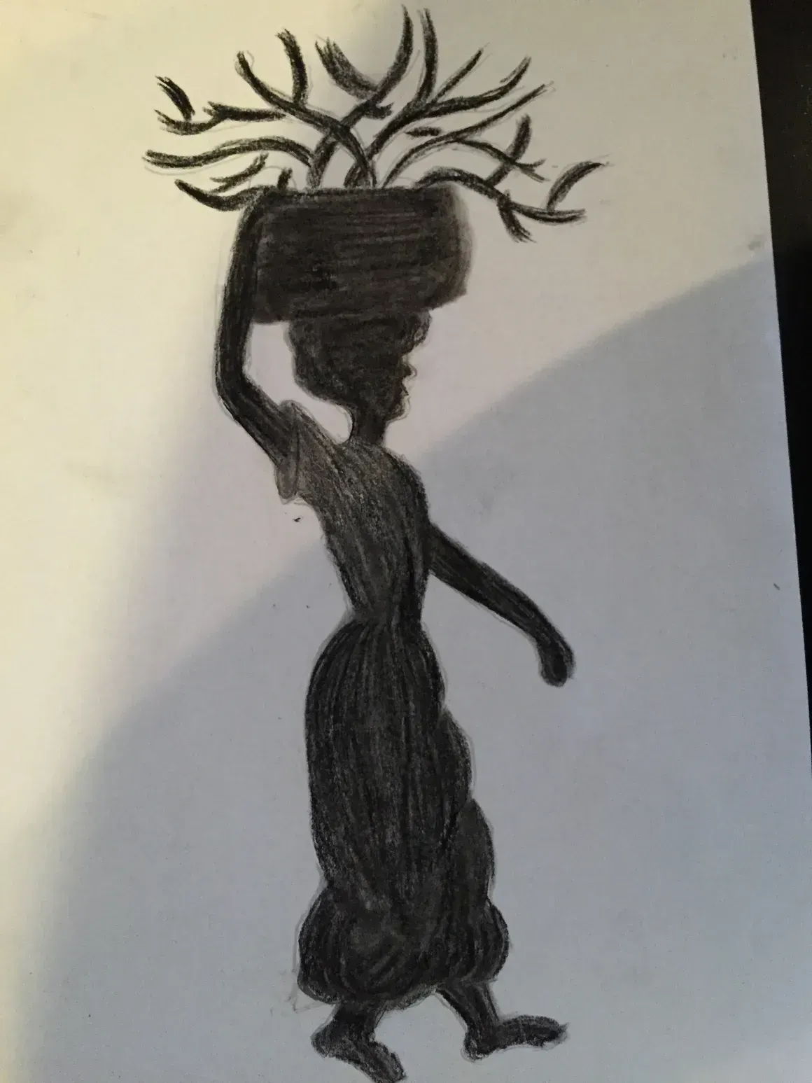 Silhouette of woman carrying basket on head with foliage.