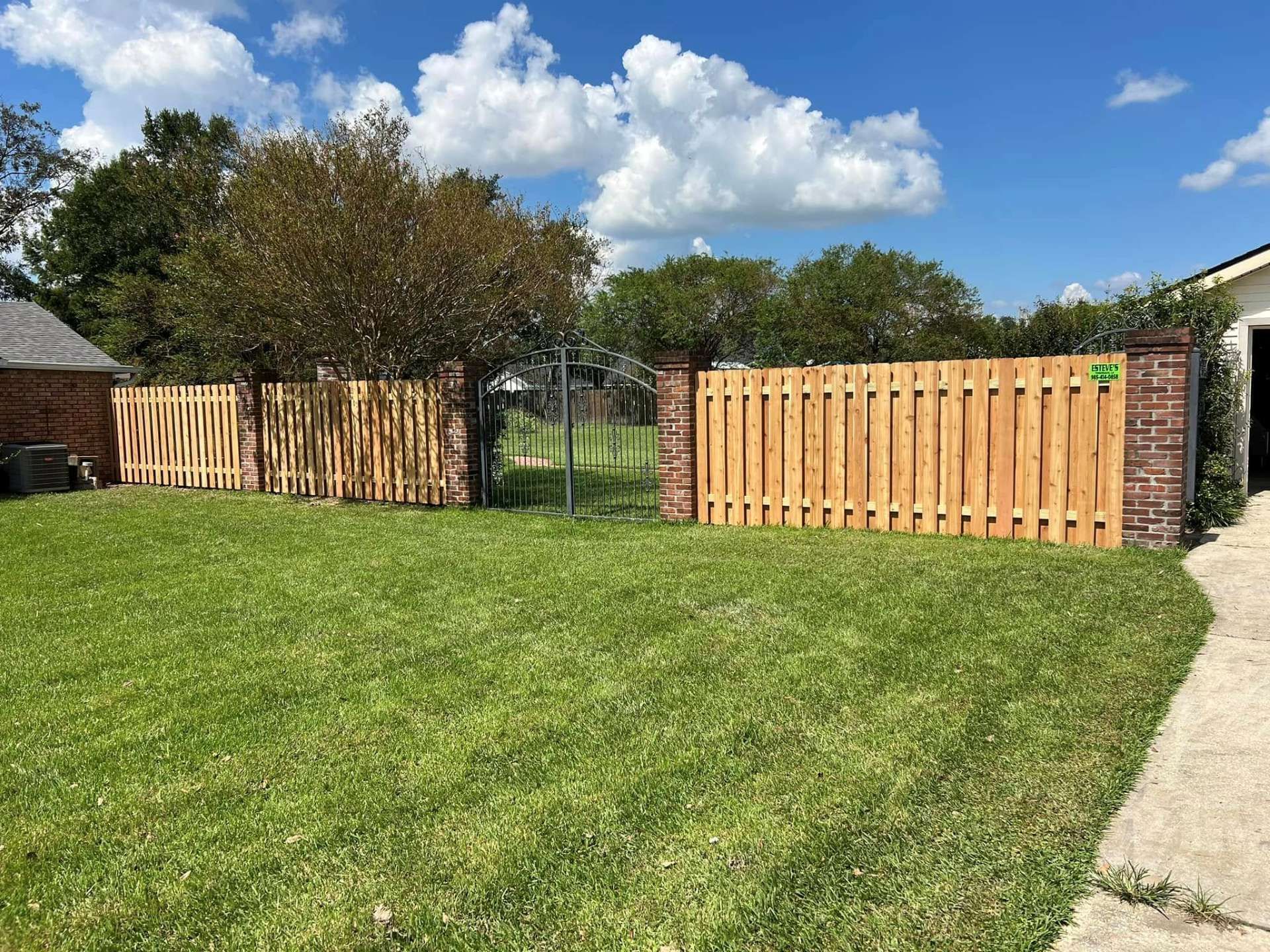 Wooden fence with brick pillars enclosing a green lawn on a sunny day.