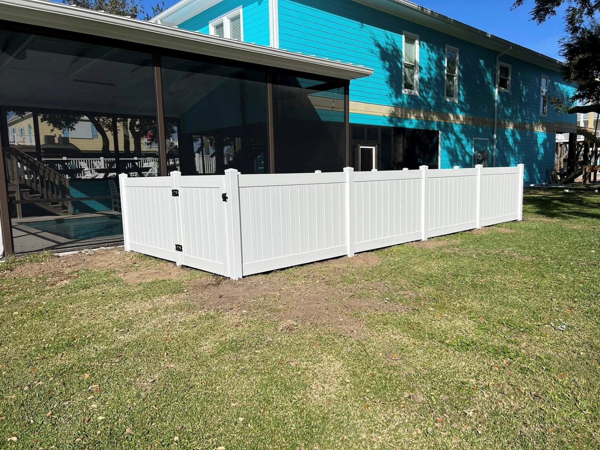 White vinyl fence in a grassy yard, beside a turquoise house and a screened porch.