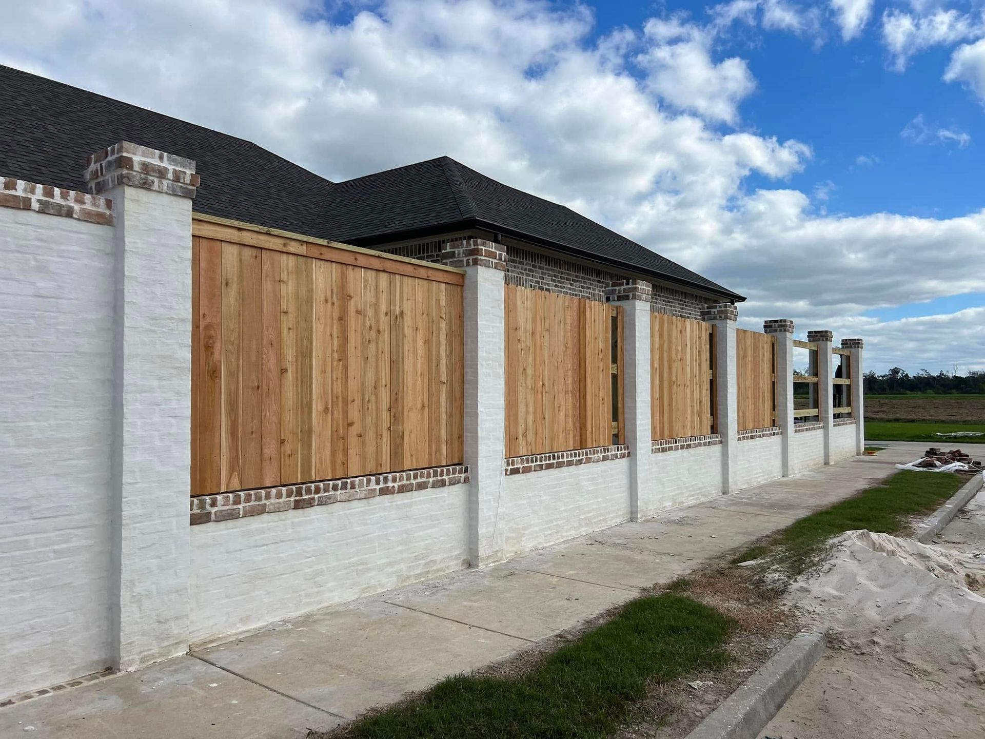 A wooden privacy fence with brick and white pillars against a cloudy blue sky.