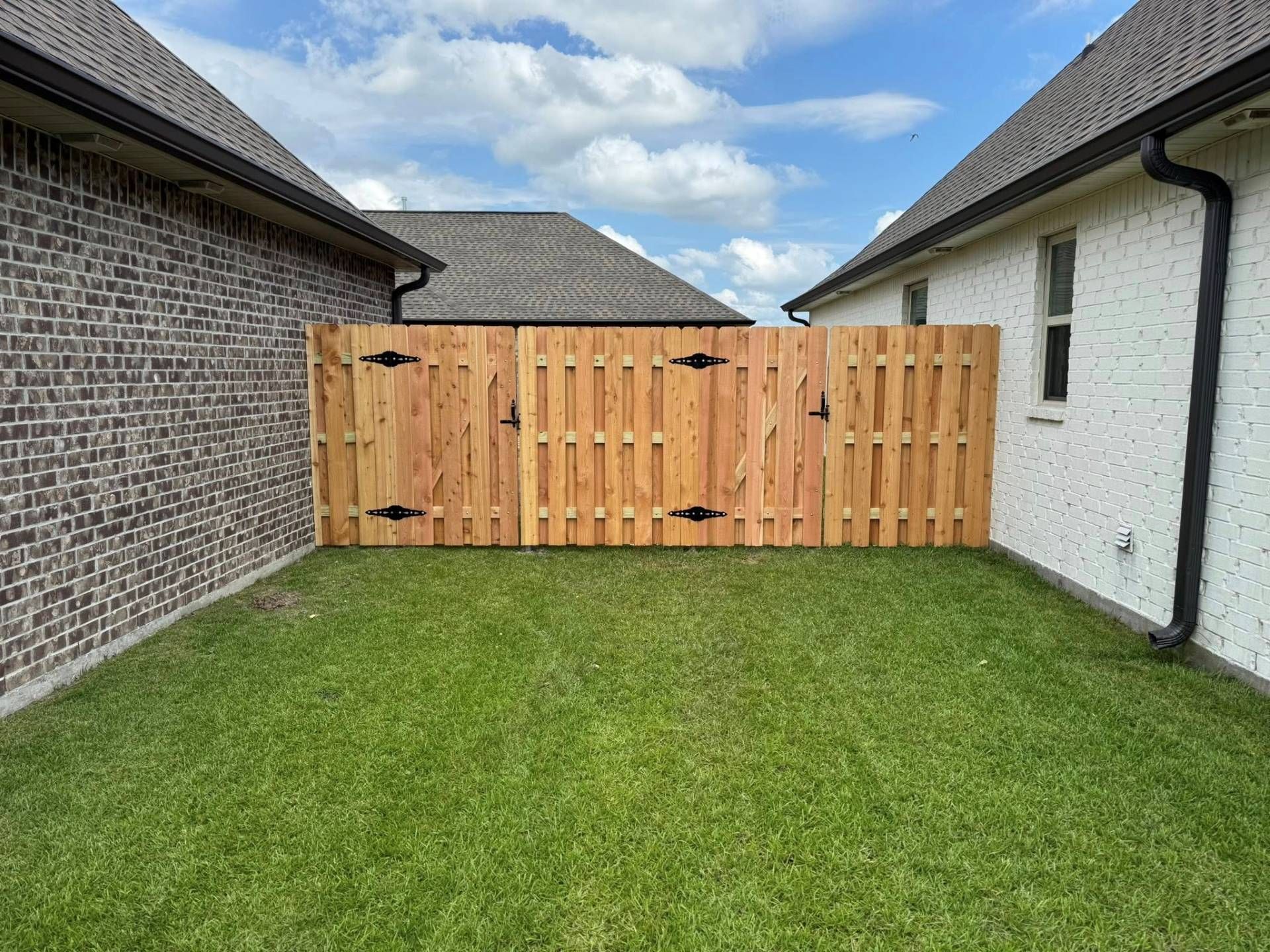 Wooden fence between two houses, separating green lawns, against a cloudy sky.