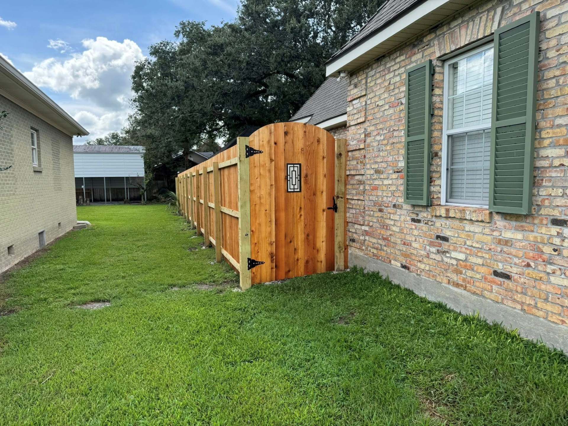 Wooden fence with gate in grassy yard between two houses.