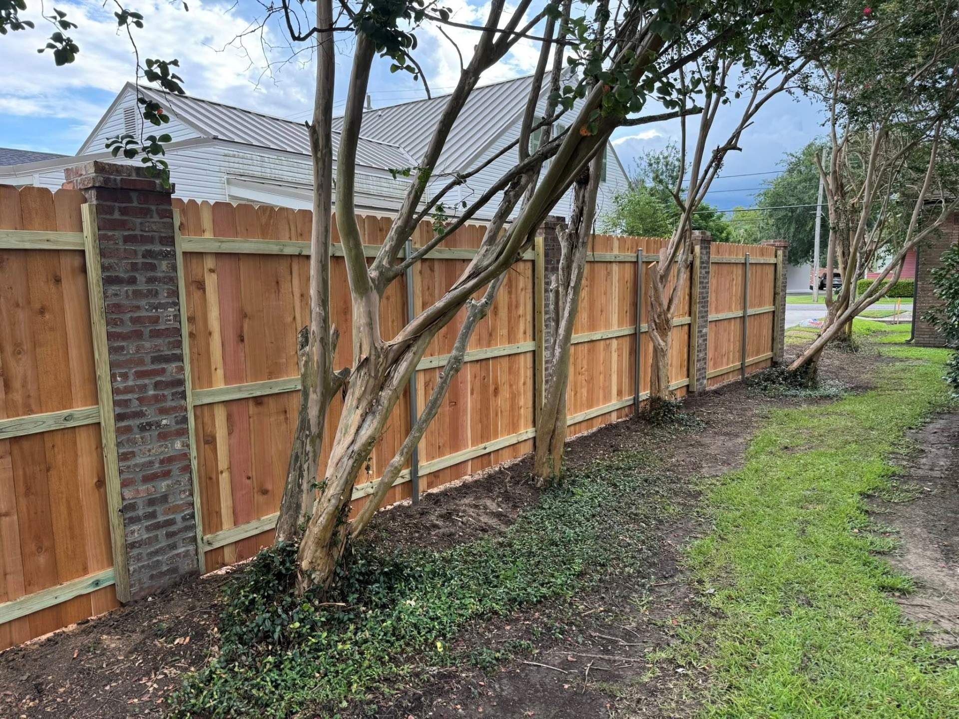 Wooden privacy fence with brick pillars and trees along a grassy yard.